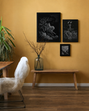 Three framed gothic black and white art prints displayed on a mustard yellow wall above a wooden bench in a styled room.