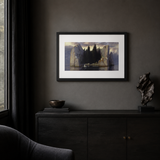 A framed art print depicting a moody landscape with tall rock formations and dark trees, displayed on a dark gray wall above a black wooden console table in a styled interior room.