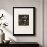 A framed vintage black and white art print with a wide white mat, hanging on a light gray wall above a dark wooden console table with a vase and bowl.