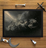 A framed dark classical painting depicting winged figures in motion, displayed on a wood-grain surface with decorative props including a bone, a small dagger, a curved blade, and a skull.